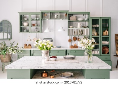 Spacious kitchen with vintage design, counter with marble top and flowers in metal bucket on it, organized furniture with various crockery, comfortable apartment interior
