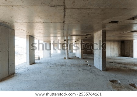 The spacious, large empty room features bare concrete walls and sturdy pillars, situated in a building that is currently undergoing the construction process, showcasing its raw architectural elements
