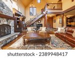 Spacious living room interior with exposed wooden beams ship like finishing wooden staircase with wrought iron hardware stone fireplace leather furniture overstuffed chairs view to dining and kitchen