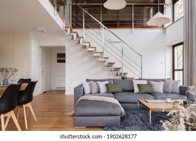 Spacious living room with nice, gray corner sofa, dining table with black chairs and with stairs to second floor