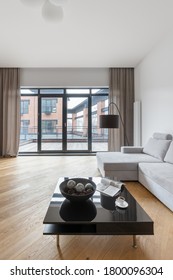 Spacious Living Room With Wooden Floor, Black Coffee Table And Gray Sofa And Big Window Wall With Balcony Doors