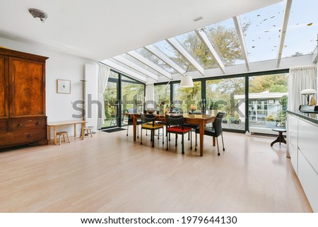 Spacious mansion kitchen room with glass walls and ceiling above wooden dining table in daylight