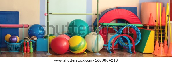 spacious modern\
gymnasium wooden floor with brightly colored fitness and gymnastic\
equipment stored near\
wall