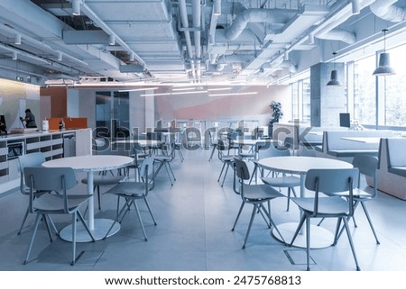 A spacious and modern office cafeteria with a versatile layout, featuring multiple round tables and chairs arranged for casual dining and meetings.