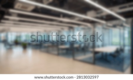 A spacious and modern office interior featuring glass-walled meeting rooms and open-plan workspaces, illuminated by bright overhead lighting.