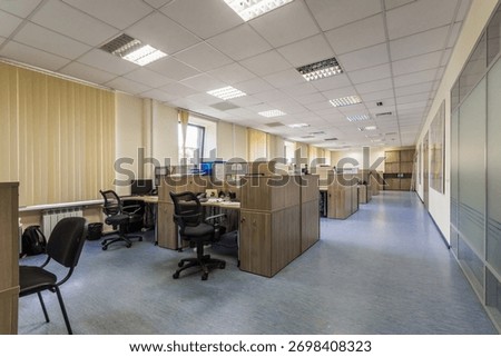 Spacious office features multiple cubicles equipped with computers and ergonomic chairs. Natural light filters through large windows