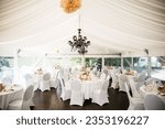 A spacious outdoor banquet tent with pristine white tablecloths and seating for a large group of people