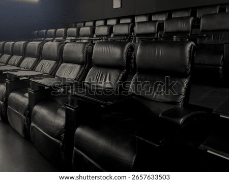 A spacious private cinema features comfortable empty black leather recliner seats, complete with individual trays and cup holders, ready for a premium film viewing