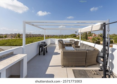 Spacious rooftop terrace featuring a comfortable wicker seating area, BBQ grill, exercise equipment, and panoramic views under sunny skies.