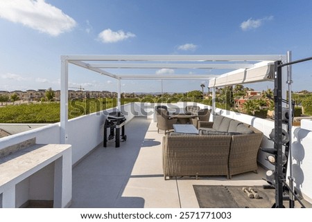 Spacious rooftop terrace featuring a comfortable wicker seating area, BBQ grill, exercise equipment, and panoramic views under sunny skies.