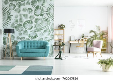 Spacious room with lamp next to blue couch against green wallpaper and pink chair near workspace - Shutterstock ID 761063926