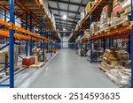 Spacious Warehouse Aisle Filled With Stacked Pallets and Boxes in Bright Lighting.The interior of a large warehouse showcases a wide aisle flanked by towering shelves stacked with pallets