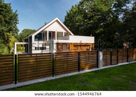 Spacious white house with wooden decoration on garage and wood style fence