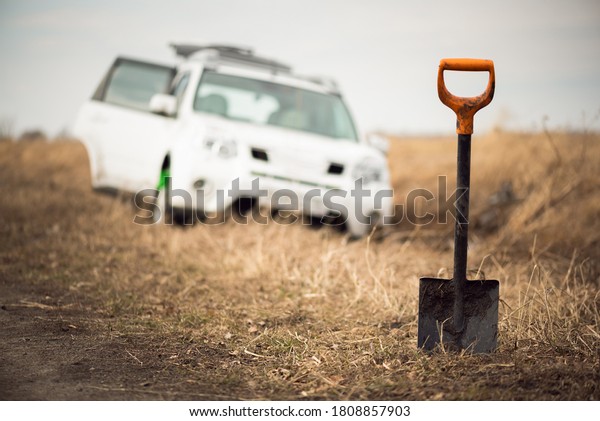 Spade in the ground on a SUV car stuck in the\
dirt background.