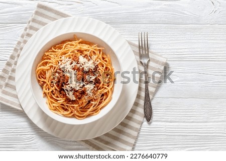 spaghetti al ragu alla Bolognese topped with shredded cheese in white bowl om white wood table, horizontal view from above, flat lay, copy space