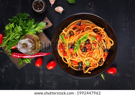 Spaghetti alla puttanesca - italian pasta dish with tomatoes, black olives, capers, anchovies and basil. Top view, flat lay