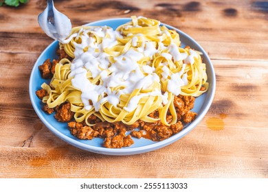 Spaghetti Bolognese pasta nests with Bechamel sauce and minced beef fried with tomatoes, onions and carrots on a blue plate on a wooden table. Top view. Copyspace or space for text. High quality photo - Powered by Shutterstock