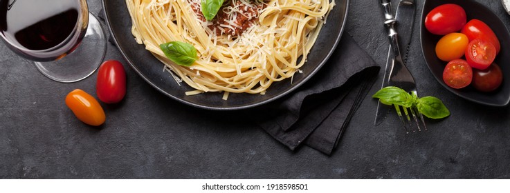 Spaghetti bolognese pasta with tomato and minced meat sauce, parmesan cheese and fresh basil and red wine glass. Top view flat lay - Powered by Shutterstock