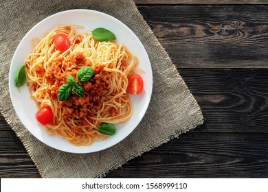 Spaghetti bolognese
				served on a white plate on a dark wooden background with tomatoes and basil