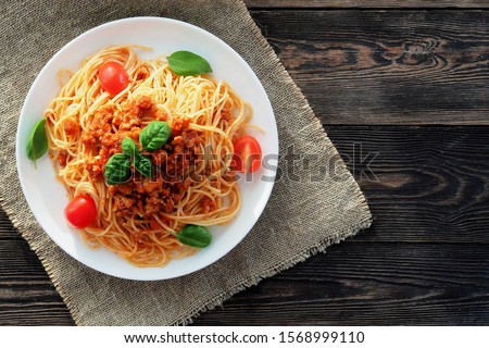 Spaghetti bolognese
served on a white plate on a dark wooden background with tomatoes and basil