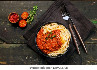 Spaghetti Bolognese with tomato sauce and thyme in black plate on wooden background. Top view