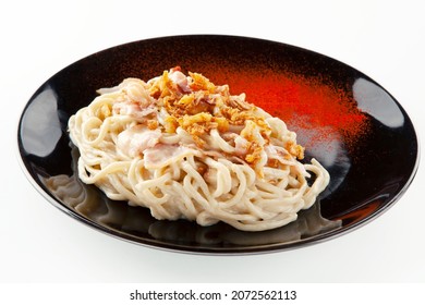 Spaghetti Carbonara With Bacon, Creamy Sauce, Fried Onion Sprinkle With Red Paprika Powder Sprinkle On A Black Ceramic Plate On A White Background