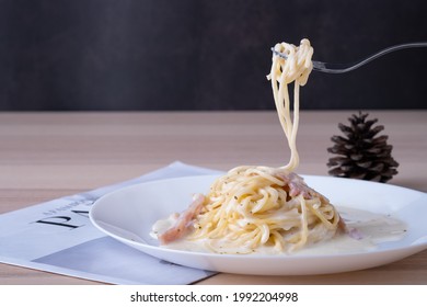 spaghetti carbonara on white plate with fork scoop up spaghetti white cream on wooden table, Italian foodmenu concept with copy space for text. 