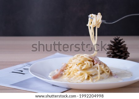 spaghetti carbonara on white plate with fork scoop up spaghetti white cream on wooden table, Italian foodmenu concept with copy space for text. 