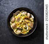 Spaghetti with clams, seafood pasta alle vongole in a black bowl. Dark background. Close up. Top view.