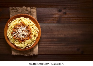 Spaghetti With Homemade Bolognese Sauce Made Of Fresh Tomato, Mincemeat, Onion, Garlic, Carrot, Served On Wooden Plate With Grated Cheese On Top, Photographed Overhead On Dark Wood With Natural Light