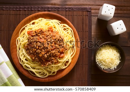 Spaghetti with homemade bolognese sauce made of fresh tomato, mincemeat, onion, garlic and carrot, grated cheese on the side, photographed overhead with natural light (Selective Focus on the sauce)