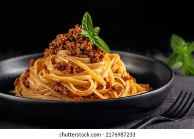 Spaghetti or linguine with meat and tomato sauce bolognese on a black plate and dark background. Close-up.