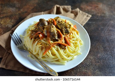Spaghetti with liver and carrots on a plate, dark textured background, with spices and tomatoes, copy space