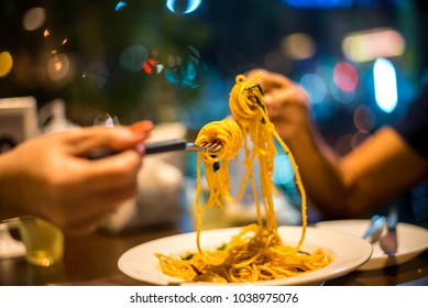 Spaghetti on a fork. Hand of two woman rolling spaghetti and keeping on a fork for eat. Beautiful colorful and light bokeh at night in the background. - Powered by Shutterstock