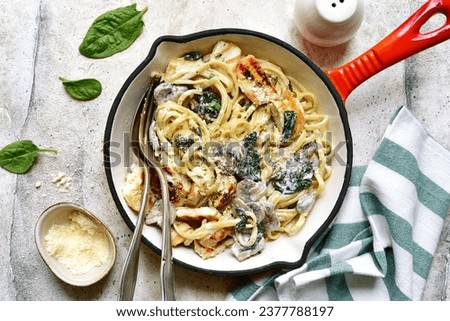 Spaghetti pasta with chicken, spinach and mushrooms in a skillet pan over light grey slate, stone or concrete background. Top view with copy space.