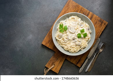 Spaghetti pasta with creamy mushroom sauce on a on wooden cutting board, gray rustic background. Italian traditional dish. Top view, copy space