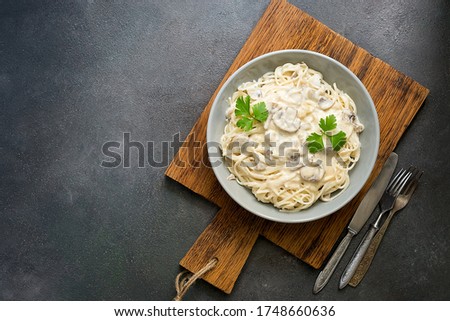 Spaghetti pasta with creamy mushroom sauce on a on wooden cutting board, gray rustic background. Italian traditional dish. Top view, copy space