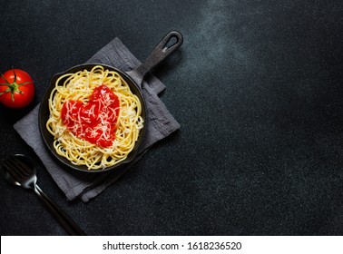 Spaghetti pasta with heart shaped tomato sauce, served in a pan. Dinner for Valentine's Day. Food with love. Top view, flat lay, black background