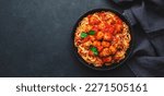 Spaghetti pasta with meatballs in tomato sauce with parsley in frying pan, dark table background, top view. Banner, copy space