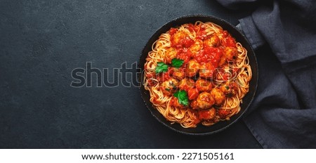 Spaghetti pasta with meatballs in tomato sauce with parsley in frying pan, dark table background, top view. Banner, copy space