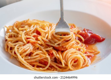 spaghetti pasta on a fork in a white plate with ketchup sauce - Shutterstock ID 2124464996