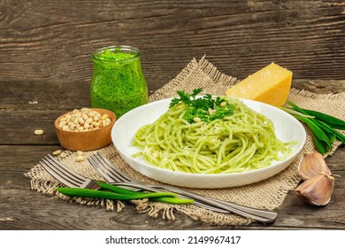 Spaghetti pasta with pesto sauce and fresh ramson leaves. Cutlery, parmesan, pine nuts. Rustic style, old wooden background, close up