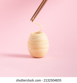 Spaghetti rolled in the shape of Easter eggs and wooden chopsticks isolated on a pink background. Minimal food concept. Square with copy space. - Powered by Shutterstock