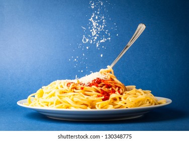 Spaghetti mit einfacher Tomate und fallender Parmesan-Käse auf blauem Hintergrund
