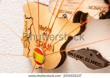 Spain flag on the pushpin with red thread showed the paths of movement or areas of influence in the global economy on the wooden map. Planning of traveling or logistic concept. Network connection. 