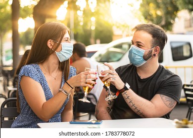 Spain Madrid. Couple toasting with beer wearing sanitary mask. Happy friends smiling with closed face masks after lockdown reopening - New normal friendship concept with guys and girls having fun