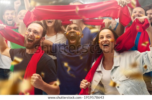 Spainian football, soccer fans cheering
their team with a red scarfs at stadium. Excited fans cheering a
goal, supporting favourite players. Concept of sport, human
emotions,
entertainment.