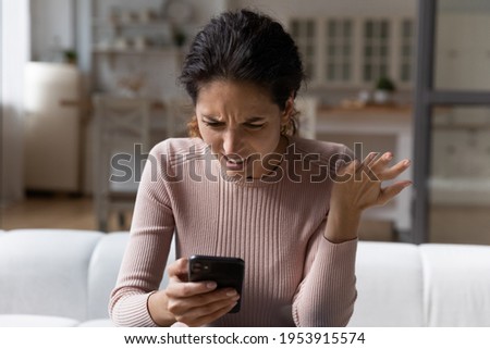 Spam mailout. Outraged nervous young latina female feel angry mad of spamming in electronic messages on smartphone. Female customer dissatisfied annoyed after reading silly email marketing letter text