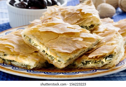 Spanakopita, Greek spinach pie with feta cheese and filo party on on plate with olives and walnuts on festive plate