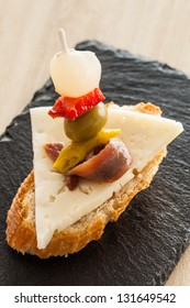 Spanish Appetizer With Cheese, Anchovy, Pepper, Olive And Onion On A Slice Of Bread Called 